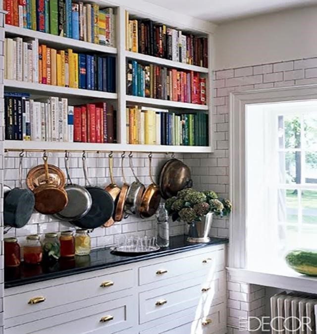 large collection of cookbooks and frypans above kitchen cabinet