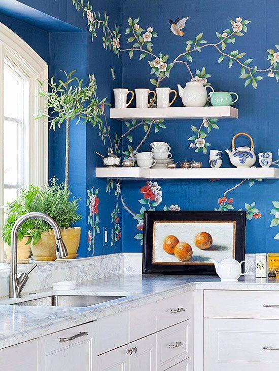 blue floral wall paper and floating shelves having with ceremic vintage, photoframe and plant on  above cabinets in kitchen
